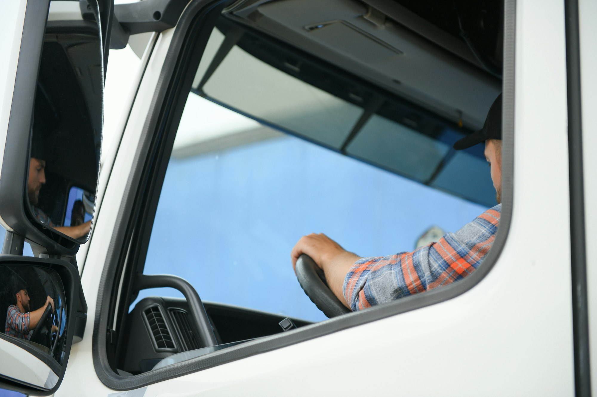 Side view of professional driver behind the wheel in truck's cabin.